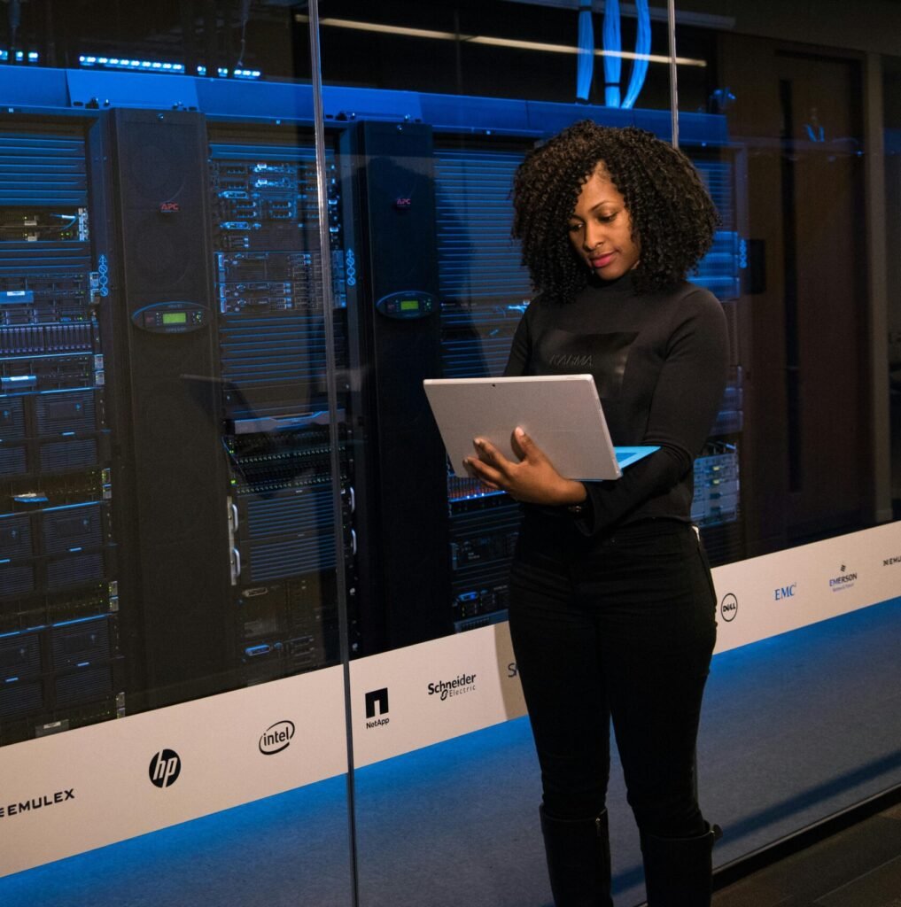 A female engineer using a laptop while monitoring data servers in a modern server room.
